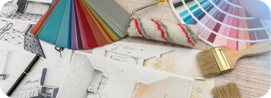 A flat lay of interior design and painting supplies, including color swatch fans, a small paint roller, paintbrushes, and floor plans.