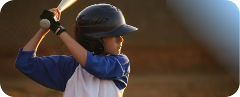 Young baseball player in a blue and white uniform and black helmet holding a bat, ready to swing.