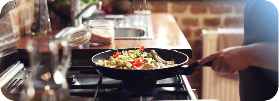 A person sautéing chopped vegetables in a pan on a gas stovetop.