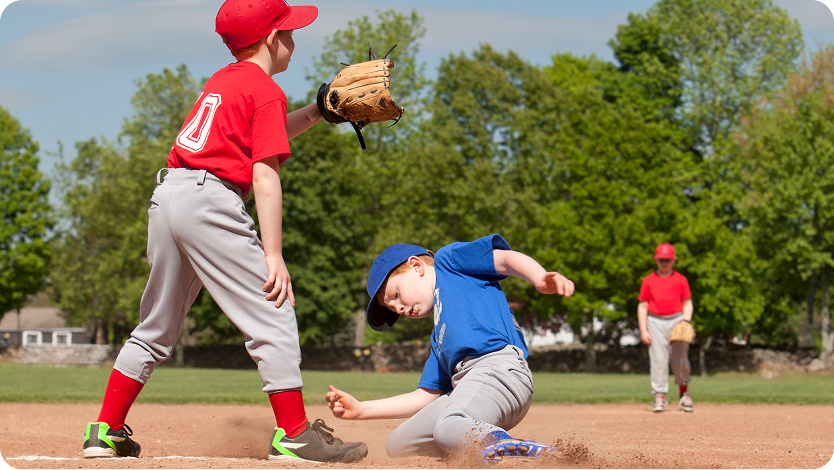 Boy in a blue shirt sliding into base guarded by another player in a red shirt during a baseball game