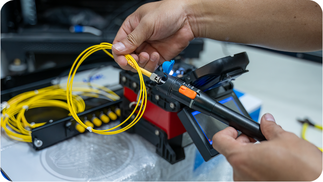 A technician inserting a coiled yellow fiber optic cable into a fusion splicer tool.