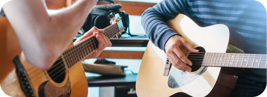 Close-up view of two people playing acoustic guitars side-by-side during a music session."