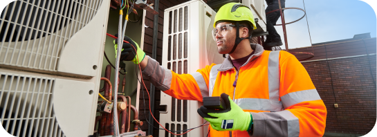 A construction and trades student in safety gear tests HVAC unit wiring with a multimeter, showcasing hands-on career training.