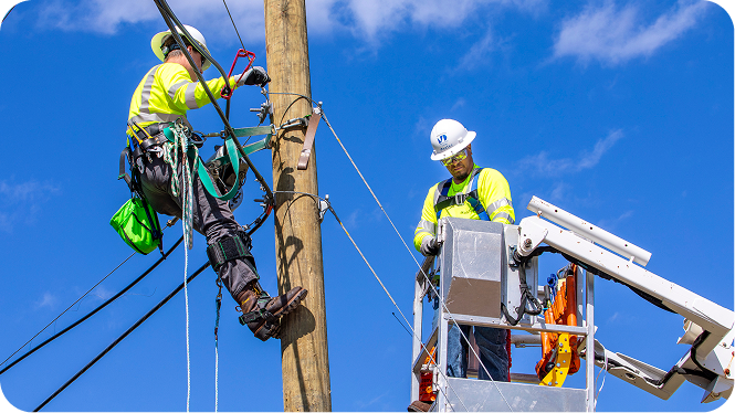Two utility workers in safety gear, one climbing a pole and another in a bucket lift, working on power lines.