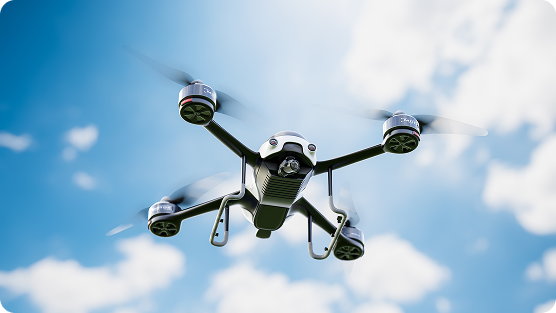 A white and black quadcopter drone flying mid-air against a bright blue sky with scattered white clouds.