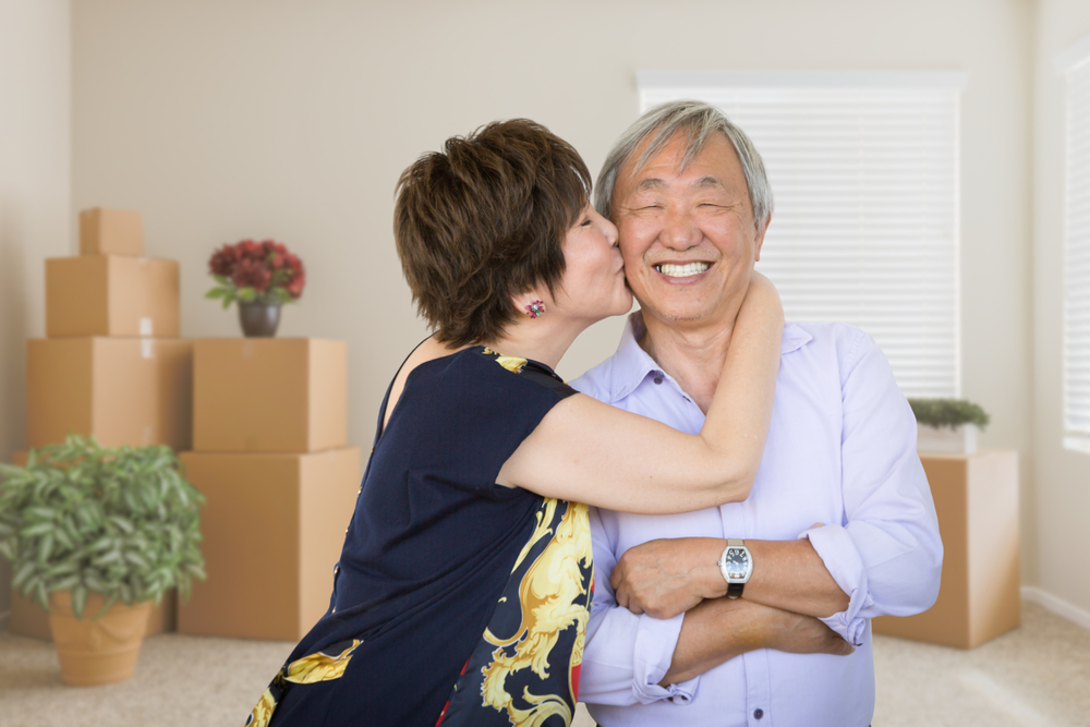 A wife kisses the cheek of her husband in front of moving boxes