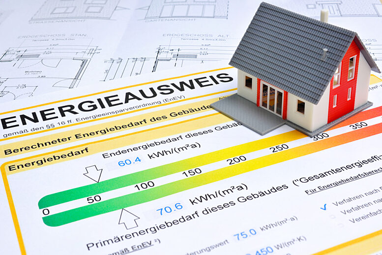 Der Energieausweis gibt sowohl den Primär- als auch den Endenergiebedarf eines Gebäudes an. Ein Energieausweis neben einem Modellhaus