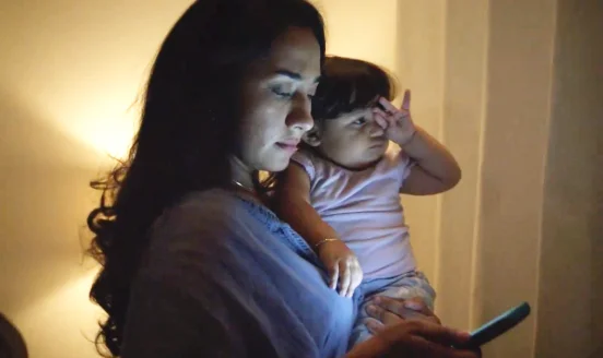 Woman holding a baby while receiving a text alert from Jambalaya News