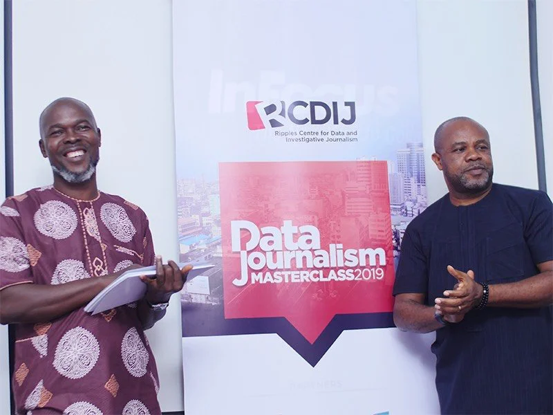 Samuel Ibemere and his colleague standing in front of a Data Journalism conference poster. They are both smiling and have their hands clasped in front of them
