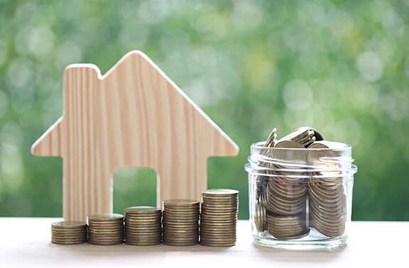 Wie viel Förderung gibt es für eine Kernsanierung? Modell-Haus aus Holz neben Geldmünzen