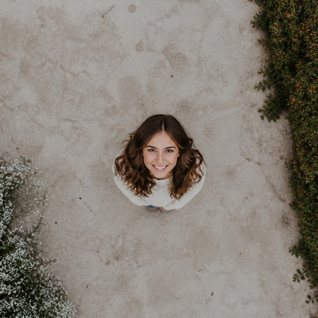 head-and-shoulders portrait of an original character: a young woman with wavy chestnut hair and a warm smile, plain soft backdrop — Aerial Drone Photography Style profile picture