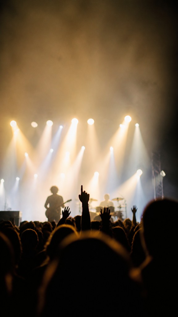 a live music scene with a glowing stage and silhouetted crowd, energetic vertical composition with open space at the top, no text — Photographic Realism Art Style flyer