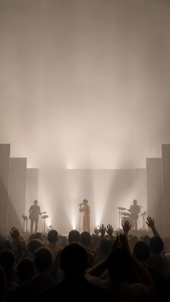 a live music scene with a glowing stage and silhouetted crowd, energetic vertical composition with open space at the top, no text — Minimalist Fashion Design flyer