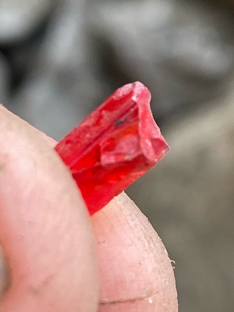 Not a diamond (appears to be a colored crystal, possibly ruby, tourmaline, or colored glass/resin given the rough, elongated prismatic crystal habit and vibrant red coloration) - Rough / Raw crystal form