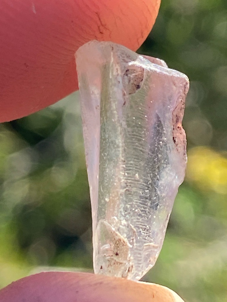 Not a diamond; this specimen appears to be an unpolished or raw crystal fragment of quartz, glass, or potentially a silicate mineral, exhibiting natural conchoidal or irregular rough surface features rather than diamond crystal faces. - Raw, uncut, irregular elongated crystal fragment.