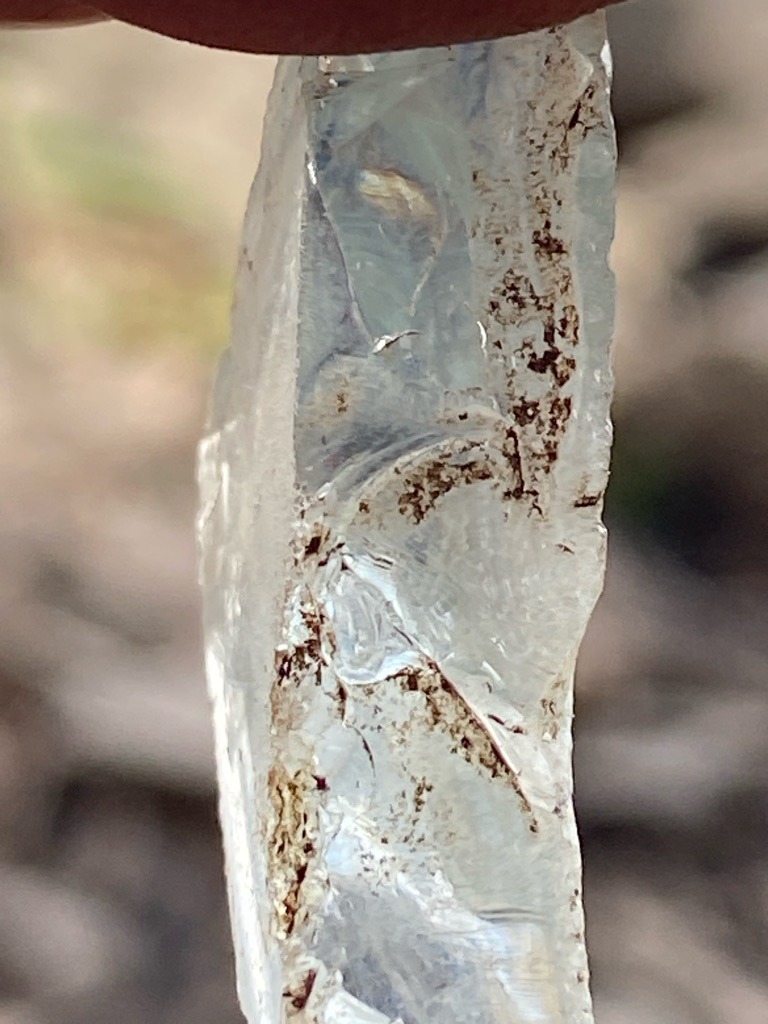 Not a diamond; this appears to be a raw, unrefined crystal or mineral shard, possibly quartz or a silicate mineral with matrix inclusions. - Rough uncut crystal shard, irregular elongated form.