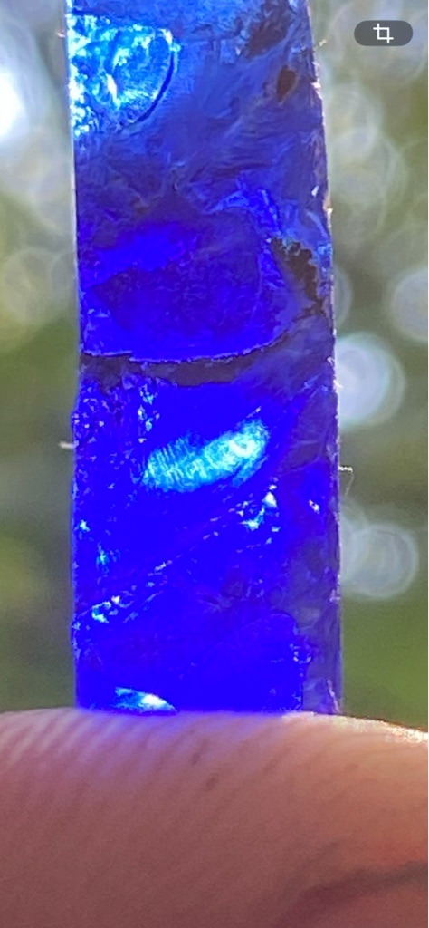Not a diamond; appears to be a raw mineral specimen, synthetic material, or colored glass illuminated by a strong blue light/laser, lacking true diamond characteristics. - Rough uncut bar / irregular elongated crystal fragment