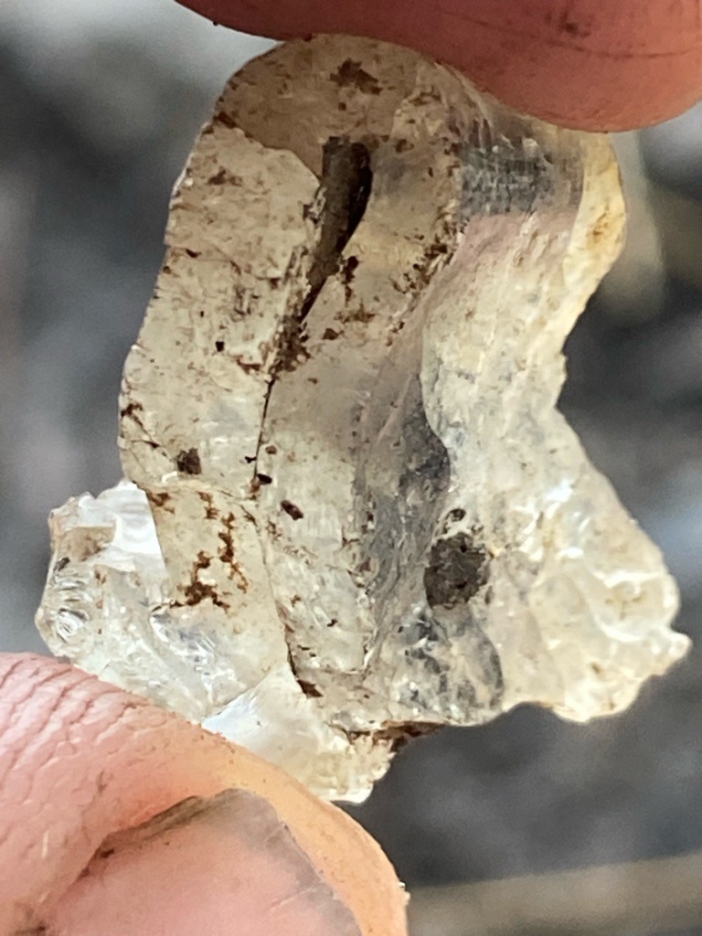 The specimen shown is a rough, unpolished mineral crystal. Based on visual characteristics, it strongly resembles rough quartz or a similar pegmatite mineral rather than a gem-grade diamond crystal. - Irregular rough crystal form, unpolished and uncut