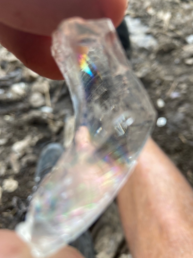 Not a diamond; this is a piece of curved clear glass or quartz exhibiting thin-film interference/fracture rainbows - Irregular raw fragment, curved shard