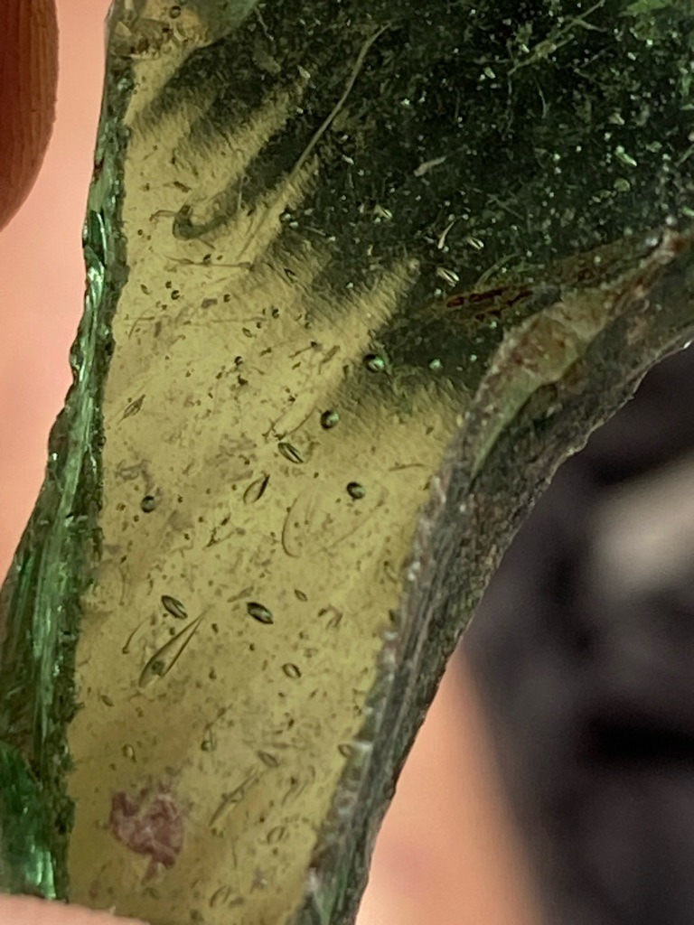 Not a diamond; this is a piece of green glass containing prominent gas bubbles and flow lines, indicative of manufactured or processed glass rather than a crystalline gemstone. - Irregular raw or broken shard, unpolished and uncut.