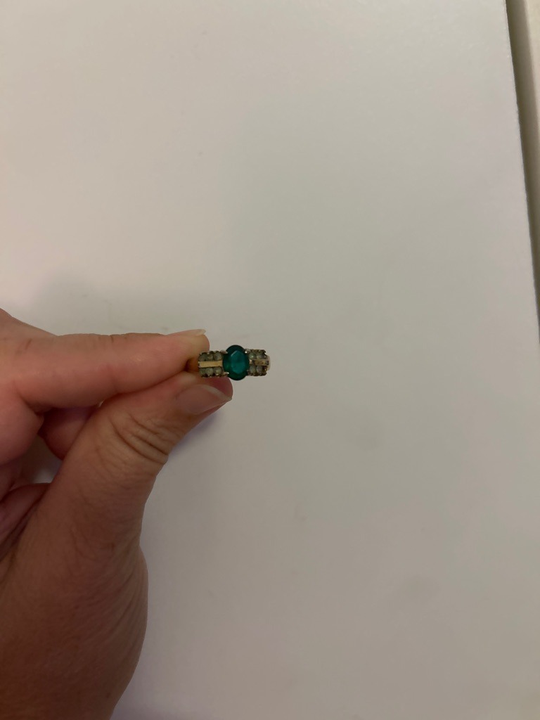 Not a diamond; the central gemstone appears to be a green-colored stone (potentially emerald or glass/synthetic spinel) mounted in a vintage-style ring with smaller accent stones. - Oval (central stone)