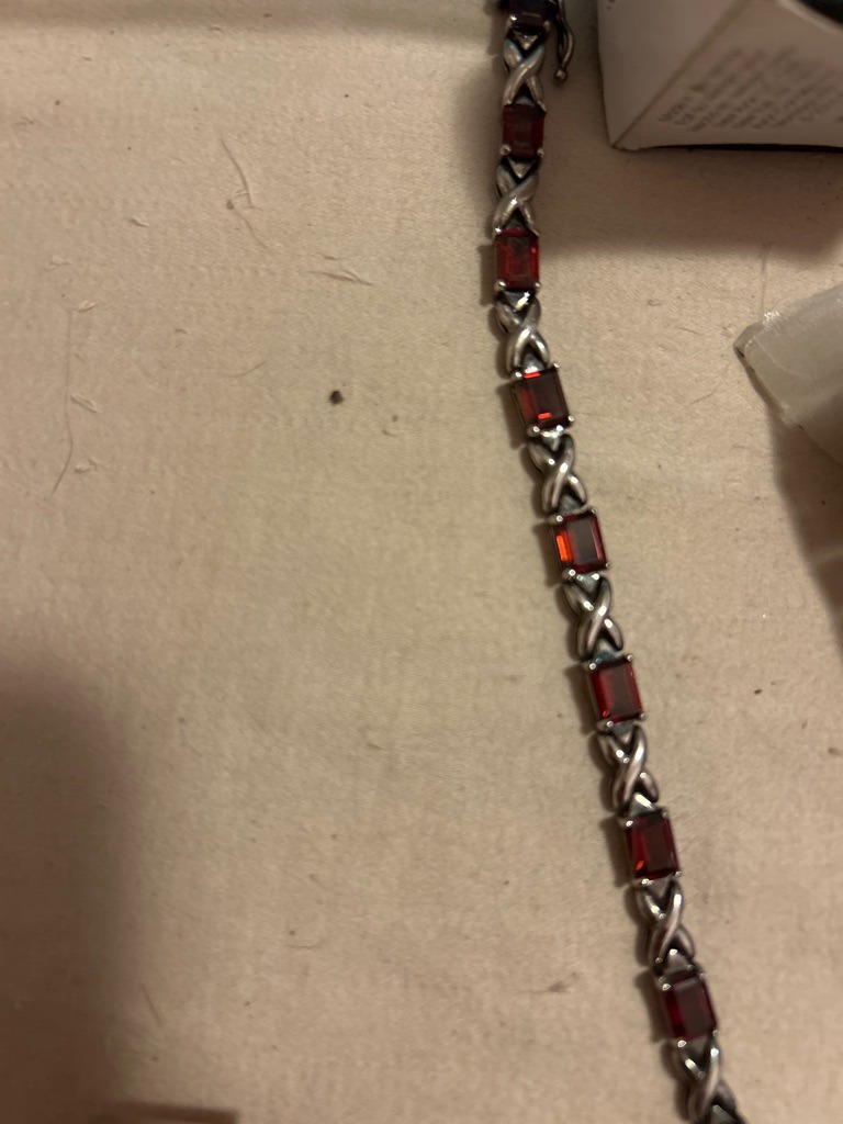 Not a diamond; the image shows a gemstone tennis bracelet featuring red-colored gemstones, likely garnets or rubies, set in an 'X and O' link motif. - Emerald cut or rectangular step-cut