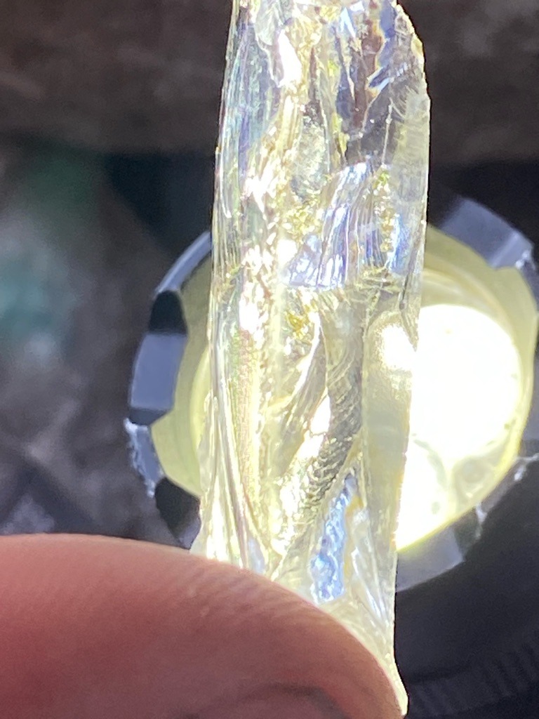 Not a diamond (appears to be a translucent crystal mineral, quartz, or resin specimen illuminated by a light source) - Rough crystal / elongated unpolished shard