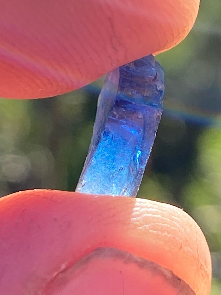 Not a diamond; this specimen is a rough mineral crystal, likely blue sapphire or tanzanite, exhibiting strong pleochroism and natural crystal striations. - Rough crystal / Uncut elongated prismatic crystal form