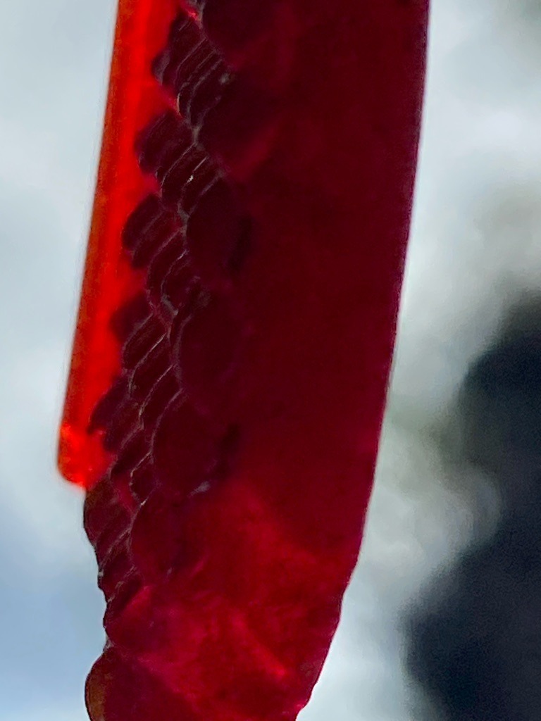 Not a diamond; the image shows a close-up macro view of a zipper or similar fastener under red lighting, completely unrelated to gemology. - Not applicable