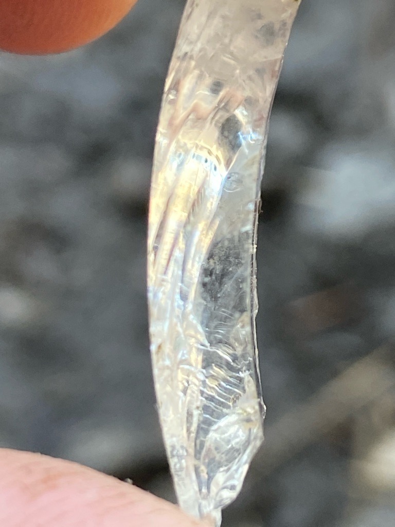 Not a diamond; this specimen appears to be raw quartz, glass, or another crystalline silicate mineral showing conchoidal fracture patterns. - Irregular raw crystal fragment / Curved shard
