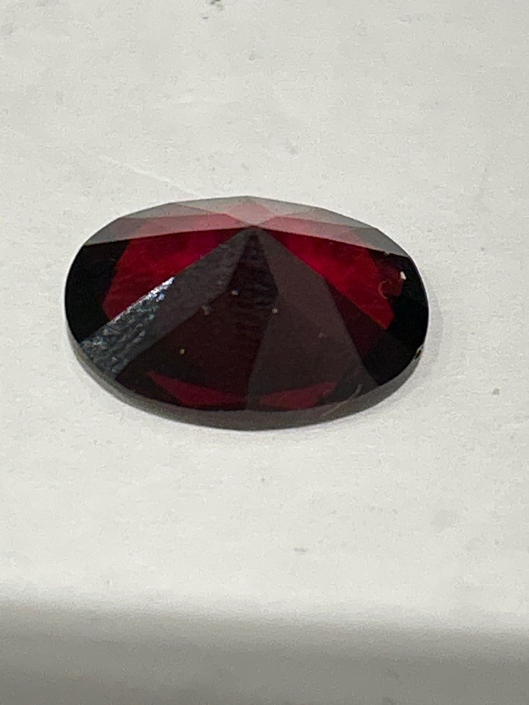 Not a diamond; appears to be a natural gemstone such as a red garnet or tourmaline based on color and faceting. - Oval Cut
