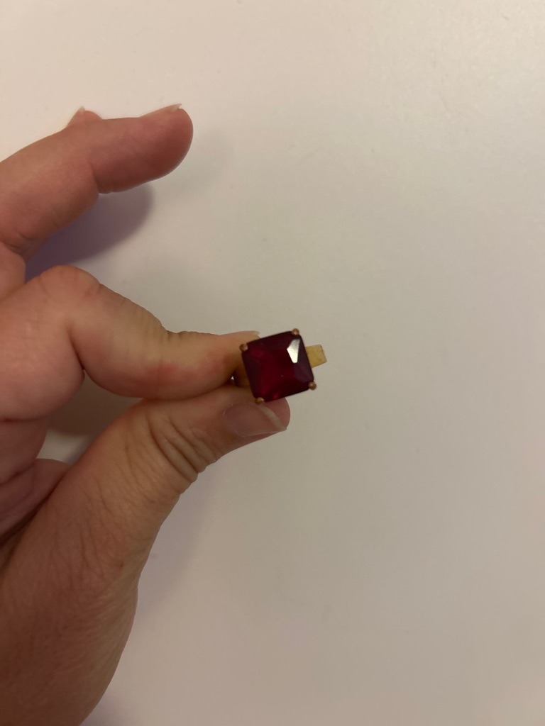 The center stone appears to be a colored gemstone, likely a synthetic ruby or red spinel, rather than a natural colored diamond, given the deep red hue and typical costume/fashion jewelry context. - Asscher or Square Emerald Cut (Step-cut square shape with cropped corners)