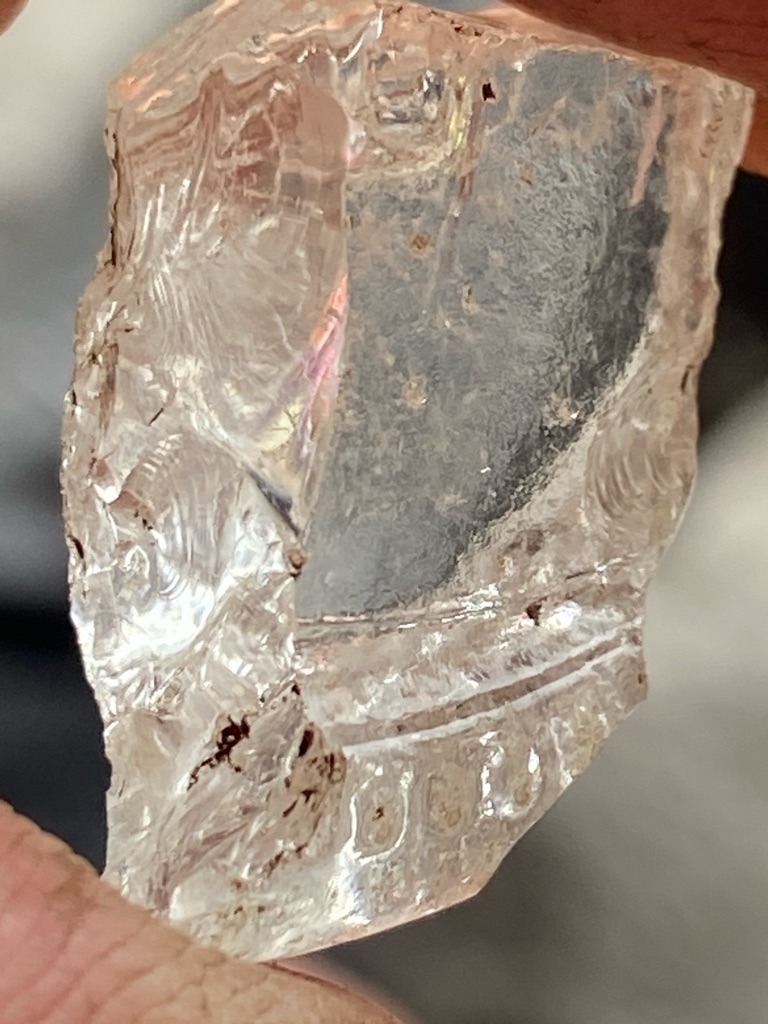 Not a diamond; this appears to be a fragment of molded or pressed translucent glass showing conchoidal fracture patterns and artifact molding details along the lower edge. - Irregular fragment (raw/uncut appearance due to fracture)