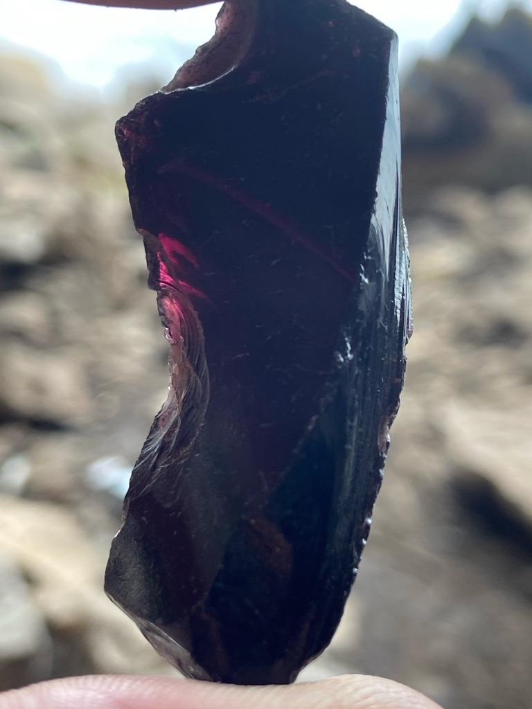 Not a diamond; this specimen appears to be rough, dark-colored glass or slag with conchoidal fracturing and internal red/purple glow when backlit. - Raw, uncut, unpolished irregular lump with natural or broken surfaces