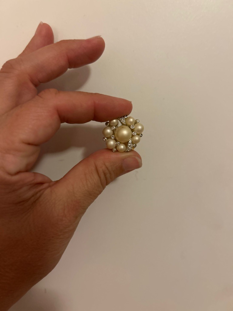 The central gem and surrounding pearls are the dominant elements, but there are accent melee diamonds integrated into the cluster setting. - Round Brilliant (for the accent melee diamonds)