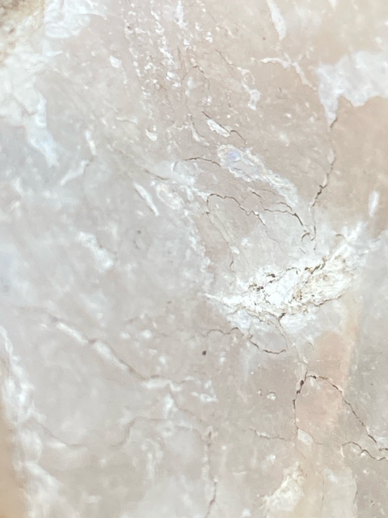 The provided image does not display a cut and polished diamond, but rather appears to be a close-up macro view of a mineral surface, potentially marble, quartzite, or raw aggregate rock showing natural micro-fractures, veining, and texture. - Not applicable; the image does not show a faceted gemstone shape.