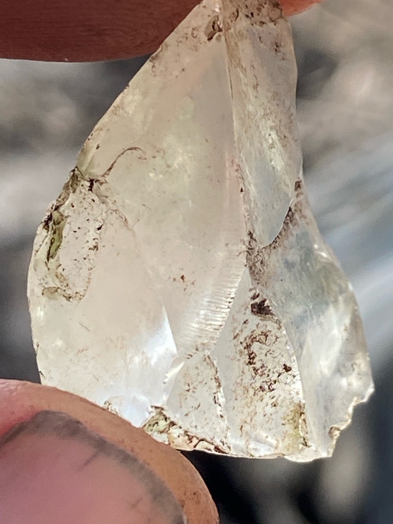Natural rough crystal / mineral specimen (likely quartz or glass given the conchoidal fractures, striations, and matrix staining, not a diamond) - Rough irregular crystal fragment with conchoidal fracture