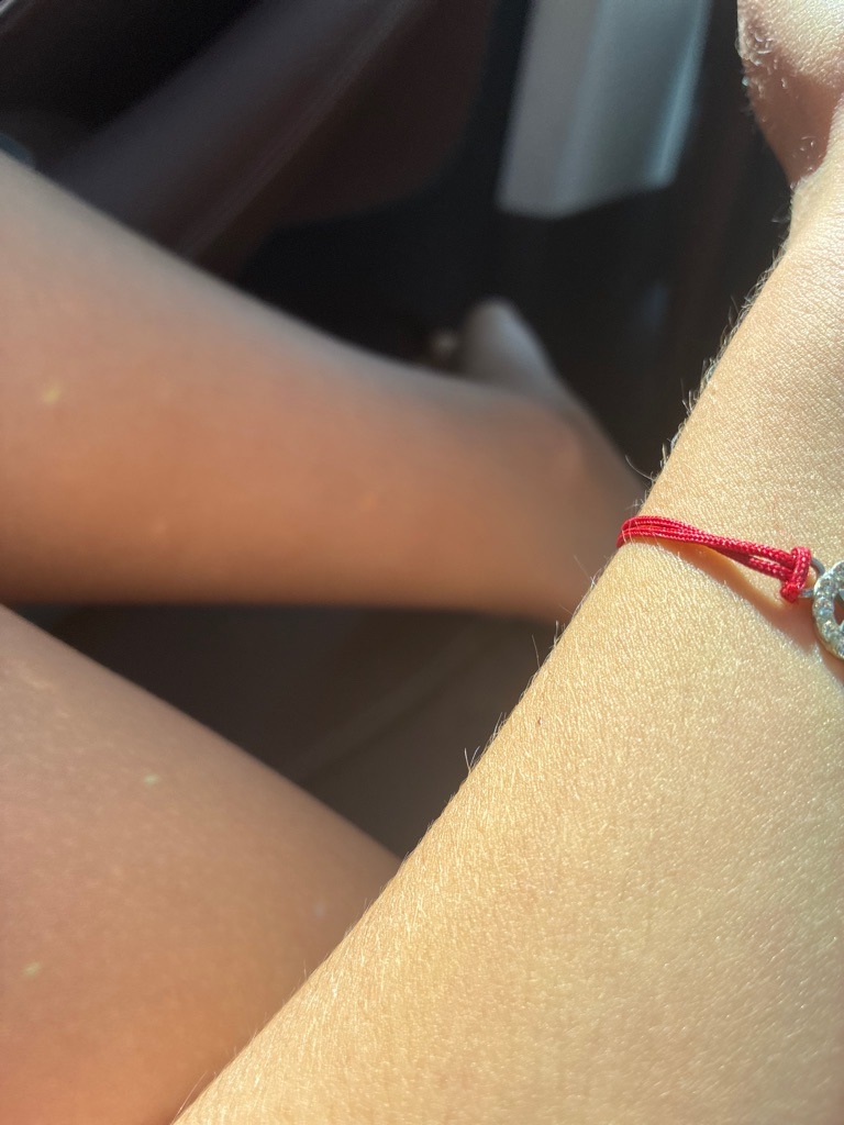 The image shows a delicate jewelry piece featuring very small accent diamonds or diamond simulants on a red string bracelet, but the stones are extremely small and indistinct due to the distance and lighting, making definitive diamond type identification impossible from this photo alone. - Round (pavé-set melee stones)