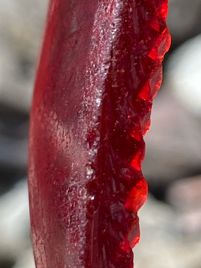 Not a diamond; this appears to be a red glass or synthetic resin material with faceted serrations, possibly a crafted artifact or tool fragment. - Irregular fragment with custom faceted edge
