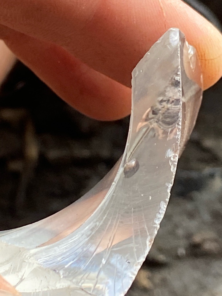 Not a diamond; this specimen exhibits conchoidal fractures, curved surface striations, and internal bubbles characteristic of manufactured glass or slag, rather than crystalline diamond structure. - Irregular fragment with curved, conchoidal fracture patterns.