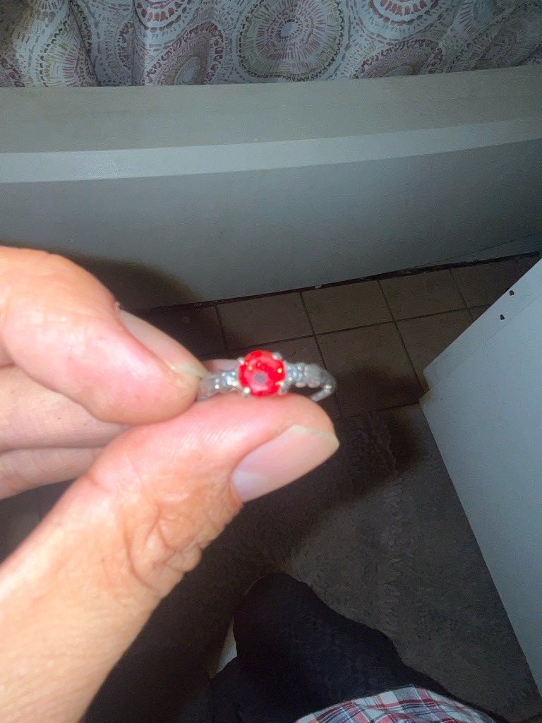The center stone appears to be a red-colored gemstone or treated diamond rather than a standard colorless diamond. It could potentially be a treated red diamond, a ruby, or a simulant mounted in a ring. - Round Brilliant
