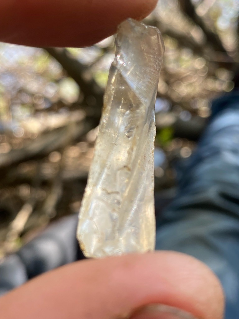 The specimen appears to be a natural mineral crystal, likely rough Quartz or a similar silicates, rather than a diamond. It lacks the isometric crystal structure (cubic/octahedral) of a diamond. - Rough / Uncut Elongated Crystal
