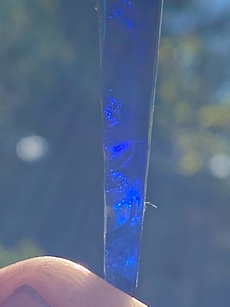 Not a diamond; appears to be an elongated mineral crystal or an icicle displaying strong blue fluorescence/inclusions under lighting. - Elongated bar or raw crystal form, non-standard diamond shape.