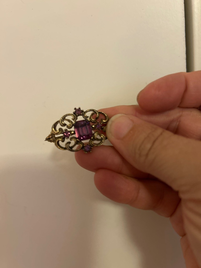 Not a diamond; this is a vintage brooch featuring purple glass or amethyst gemstones set in brass or base metal. - Emerald cut (rectangular) for the central stone and round for the accent stones.