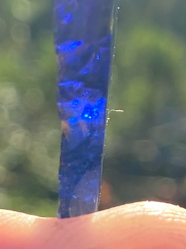 Not a diamond; this specimen appears to be an uncut, elongated mineral crystal or gemstone rough, potentially a sapphire, tanzanite, or opal showing intense blue play-of-color/fluorescence. - Rough crystal / Uncut elongated crystal form