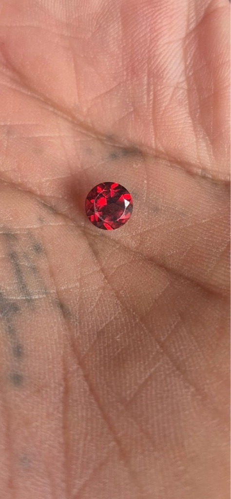 The gemstone shown in the image is not a diamond; it appears to be a red-colored gemstone such as a synthetic ruby, garnet, or spinel, rather than a natural or lab-grown diamond. - Round Brilliant