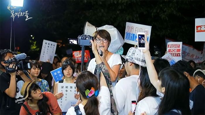 ▲ 시위 현장에서 발언하고 있는 나가무네 하나미(실즈 멤버), 안보법 반대 시위를 주도 하지만 시위 현장 밖에서는 여가활동도 즐기는 평범한 여학생이다. 