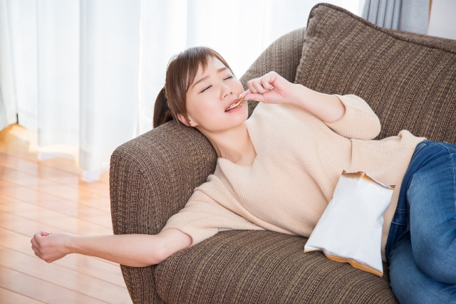 ソファに寝転んでお菓子を食べる女性