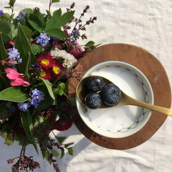 Milchkaffee mit Löffel Blaubeeren neben kunterbuntem Gartenstrauß