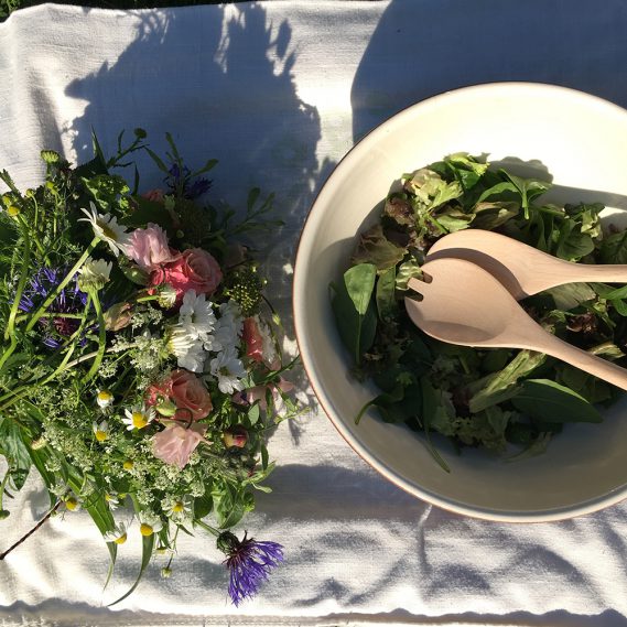 Salatbett in Salatschüssel mit Salatbesteck und Blumenstrauß